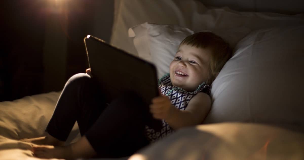 Toddler using an iPad laying on a bed.