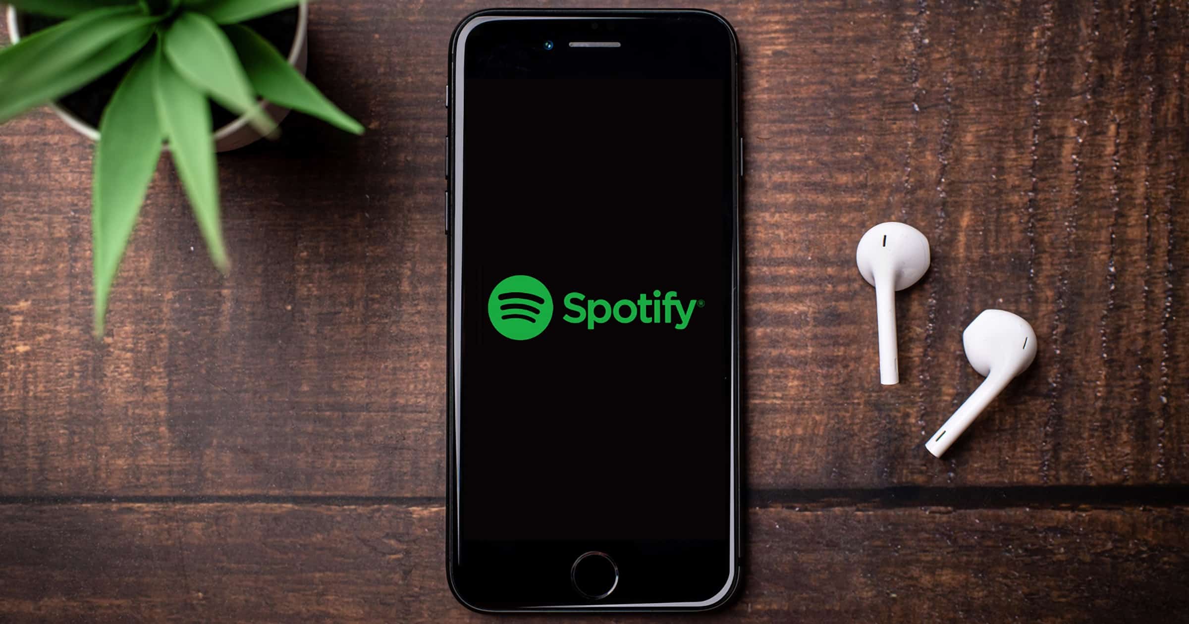 iPhone on a table with airpods and the Spotify logo.