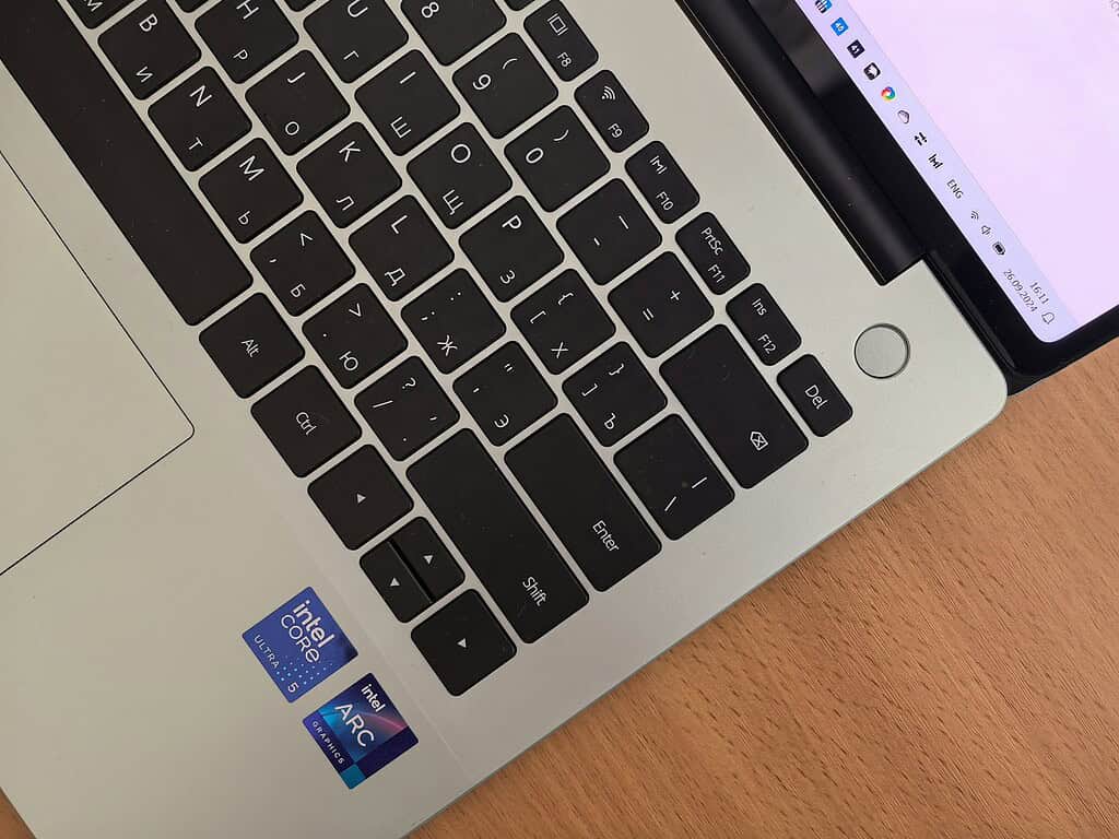 Close-up of a laptop keyboard featuring Cyrillic characters and Intel stickers on a smooth surface, with a screen visible in the background.