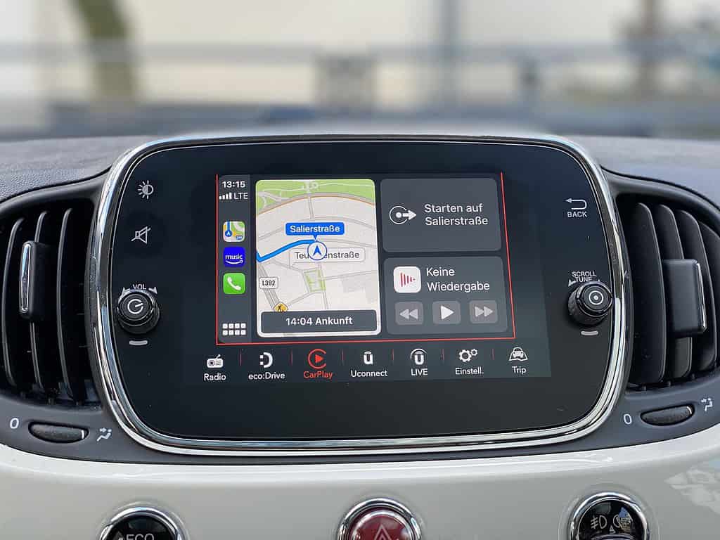 Car dashboard display showing navigation map with route directions, music options, and various multimedia controls.