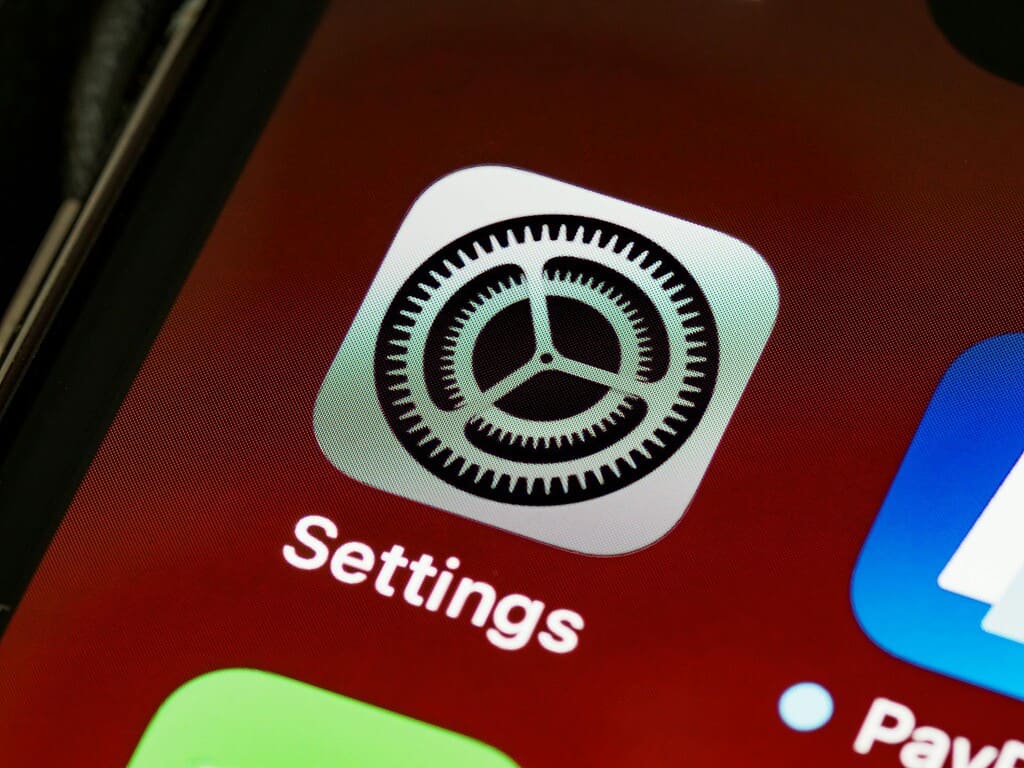 A close-up view of a smartphone screen featuring the Settings app icon with a gear design, set against a colorful background.