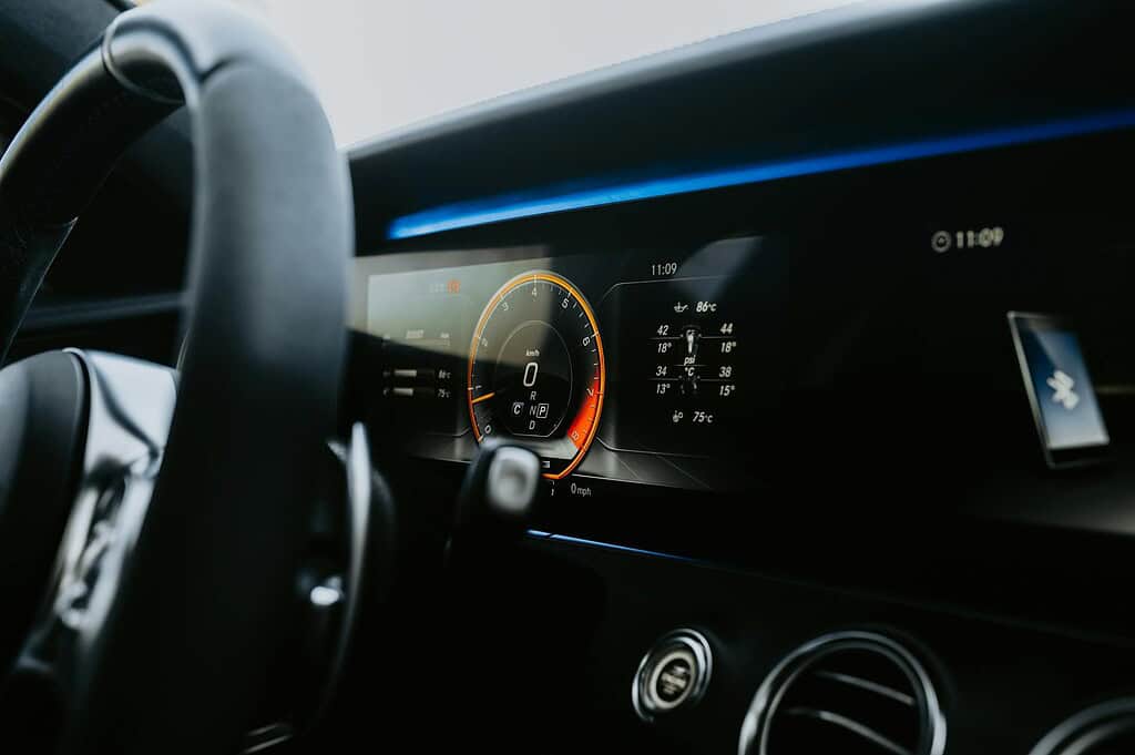A close-up view of a car's dashboard, featuring a modern digital display with speed, temperature, and various gauges.
