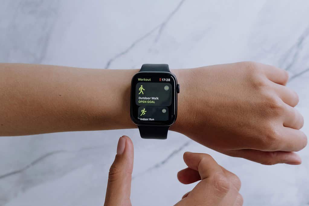 A close-up of a hand with an Apple Watch displaying workout options: 'Outdoor Walk' and 'Indoor Run', against a marble background.