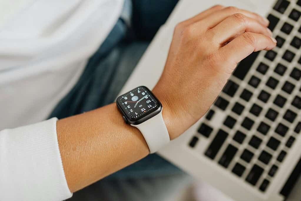 A close-up of a person's wrist with a white smartwatch, typing on a laptop keyboard, focused on technology and productivity.
