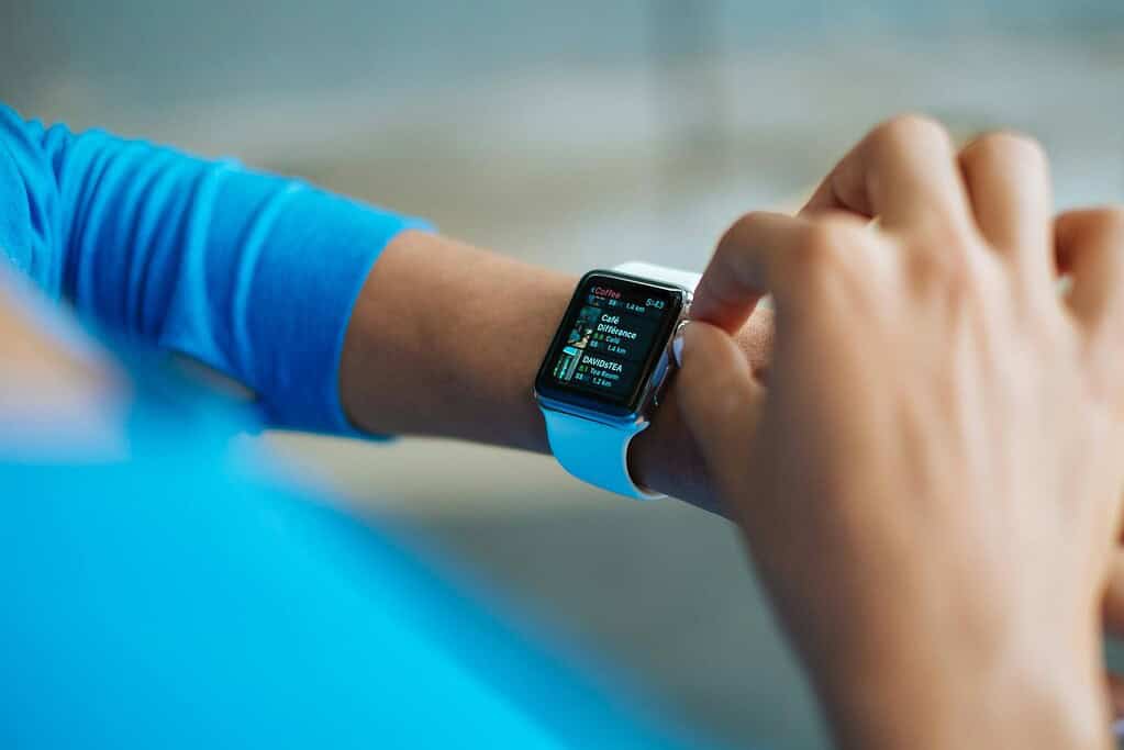 A close-up of a person checking their smartwatch displaying coffee shop details, with a blue sleeve in the background.