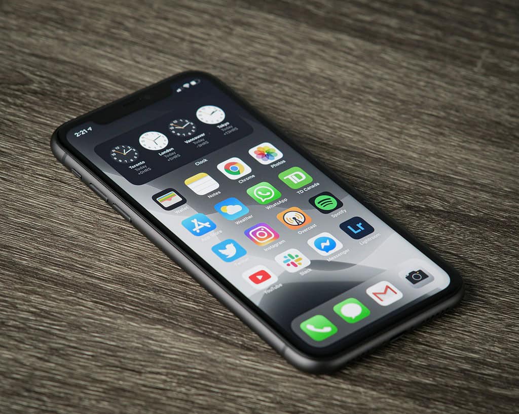 Close-up van een smartphone die verschillende app-iconen en vier wereldklokken voor Toronto, Londen, Vancouver en New York toont op een houten ondergrond.