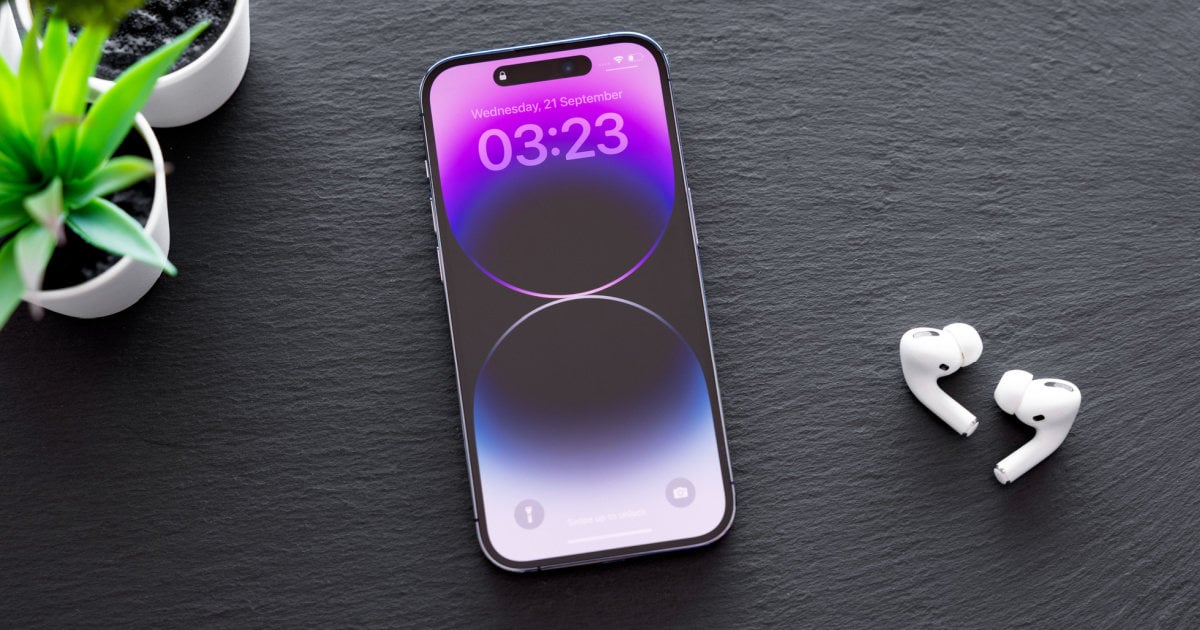 An iPhone with a purple and blue gradient lock screen displaying 03:23, placed on a dark slate surface beside white AirPods and a small potted plant.