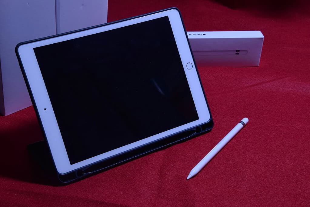 A white tablet in a black case with a stylus on a red surface, with a minimalistic white box in the background.