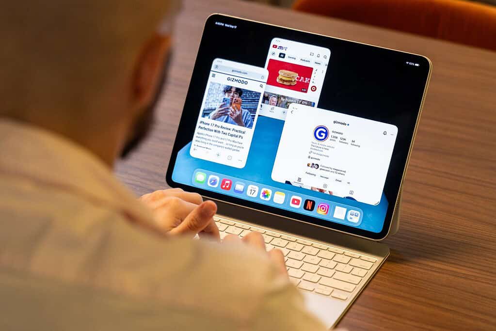 Persoon die iPad gebruikt met toetsenbord, multitasking met meerdere open vensters, browst Gizmodo artikelen en sociale media op een houten bureau.