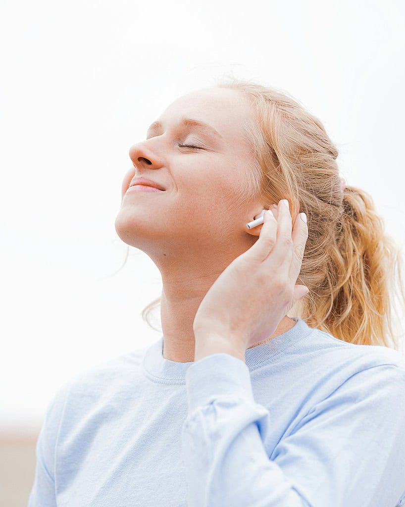 A person in a light blue long-sleeve shirt is holding their phone to their ear, looking upwards against a bright, cloudy sky.