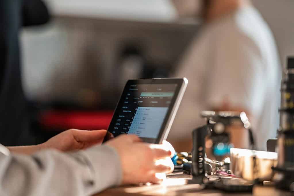 A person uses a tablet displaying a digital interface, surrounded by various tools and equipment in a workshop setting.