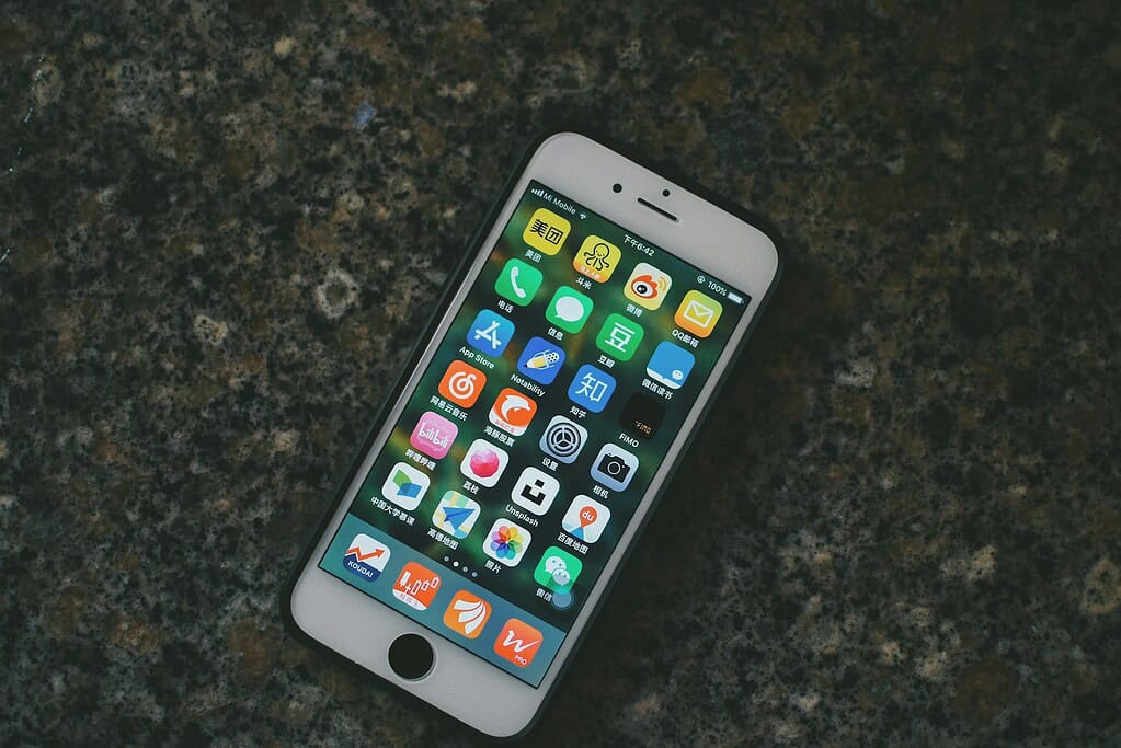 A smartphone displaying various colorful app icons on a dark, textured surface. Battery at 100% and time shows 8:42.