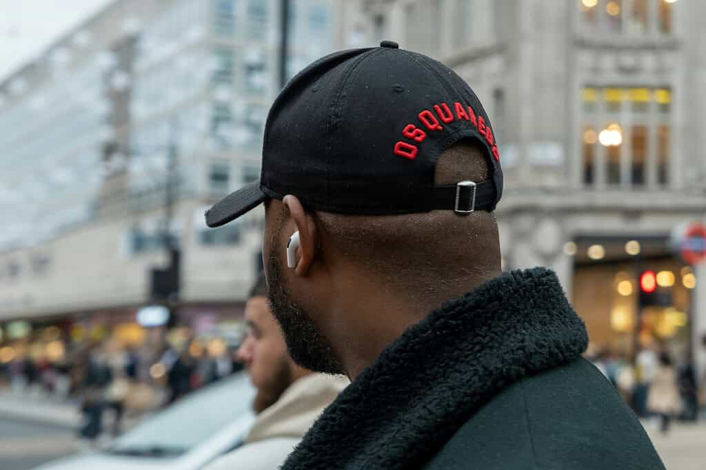 A man wearing a black hat on the street with some AirPods on.
