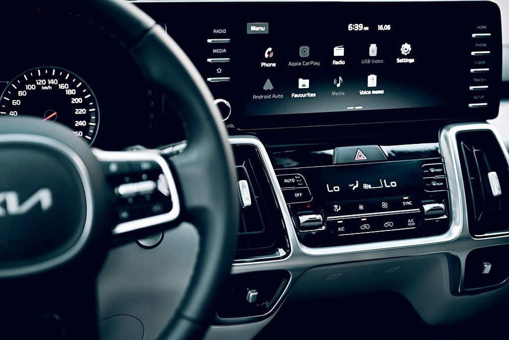 Close-up of a car dashboard featuring a digital speedometer, touchscreen interface with navigation and media options, and climate controls.