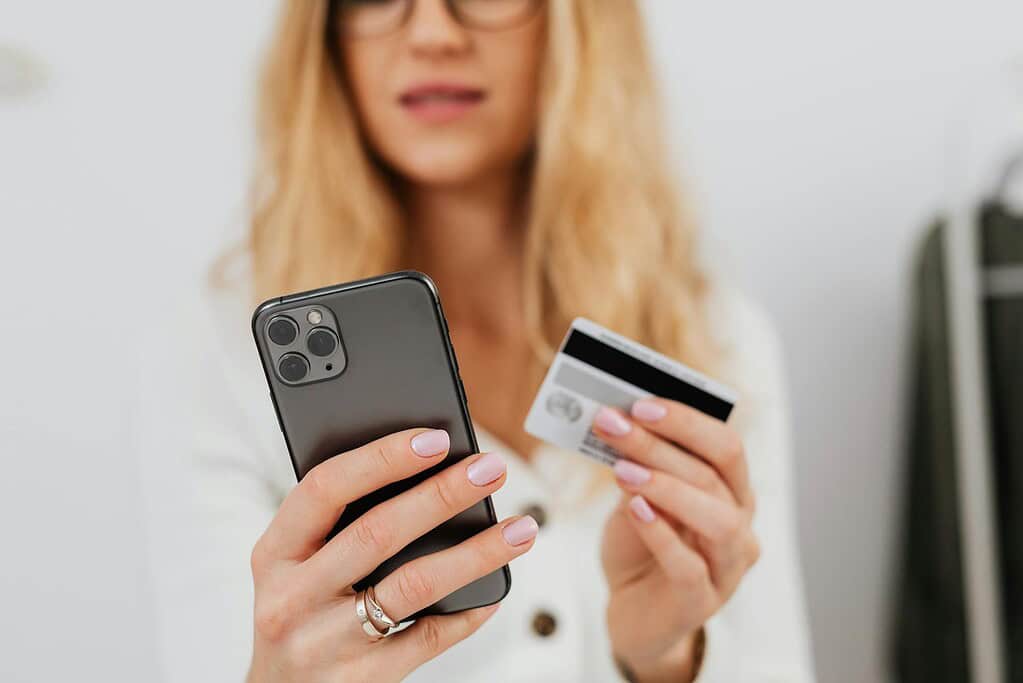A person holds a smartphone in one hand and a credit card in the other, preparing for an online transaction.