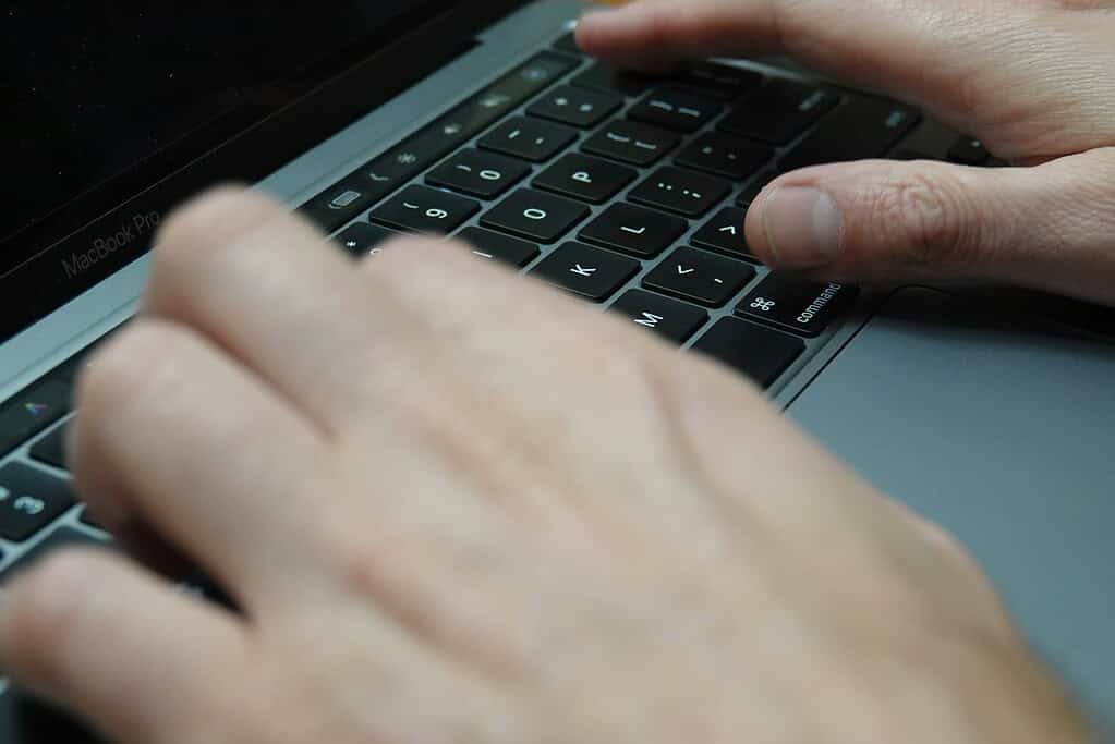 Close-up of hands typing on a MacBook Pro keyboard, with fingers positioned over the command and letter keys.
