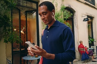 A person smiles while browsing on iPhone 17 outdoors