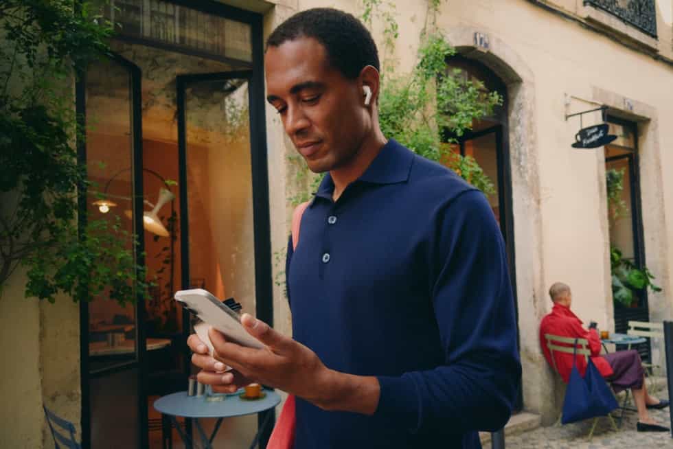 A person smiles while browsing on iPhone 17 outdoors
