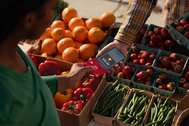 A shopper taps a contactless card on a seller iPhone at a produce stand